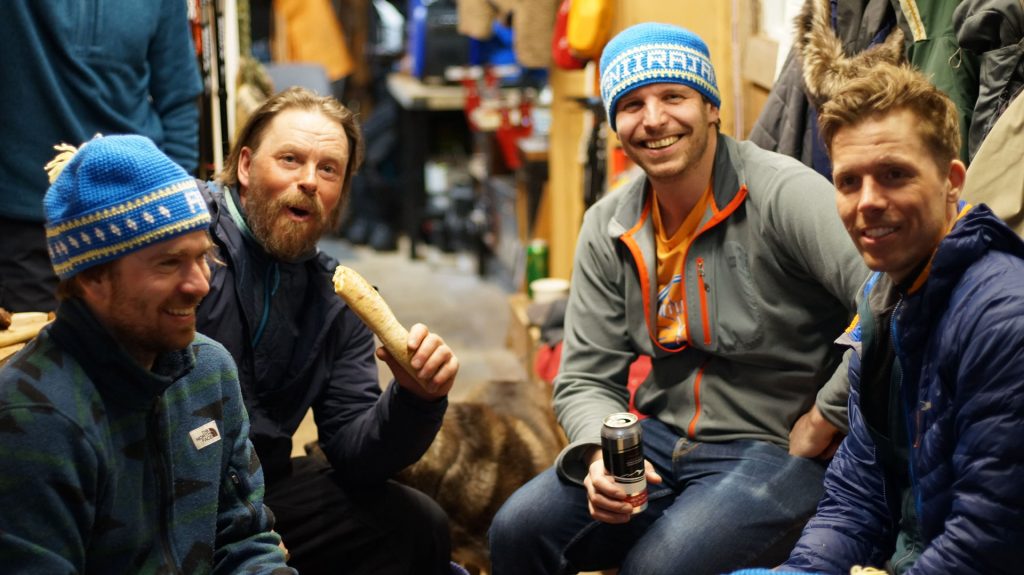 Four men smiling indoors, casual atmosphere.