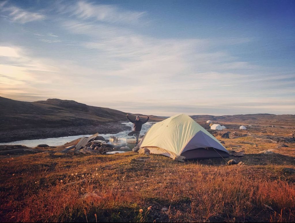 Tent by river in wilderness landscape.