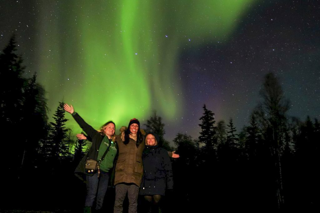 Three people under northern lights.