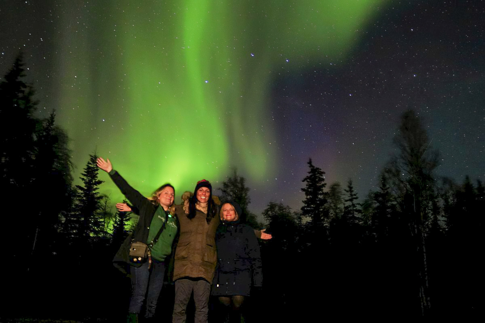 Three people under northern lights.