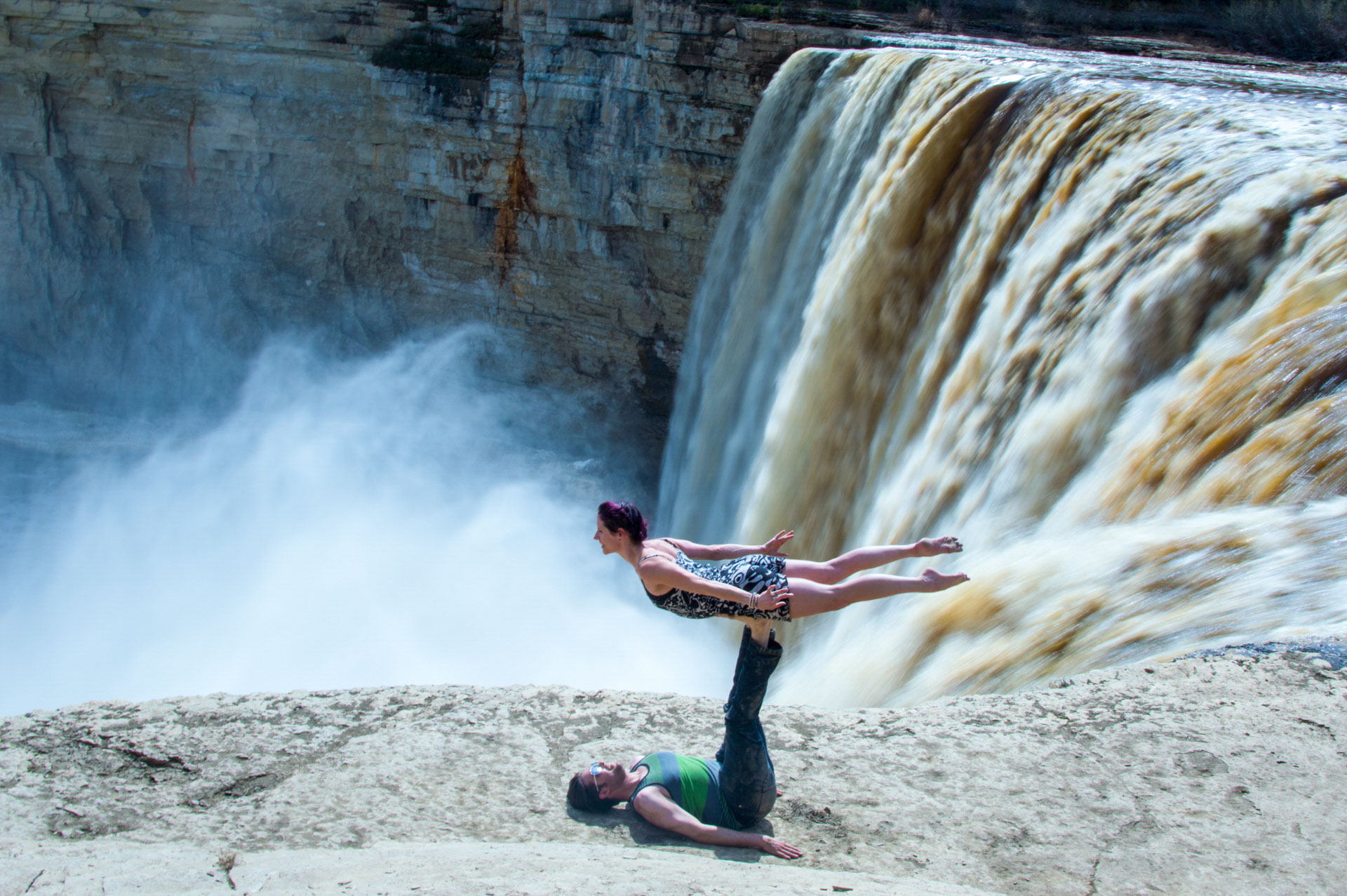 Couple performing acrobatic pose by waterfall