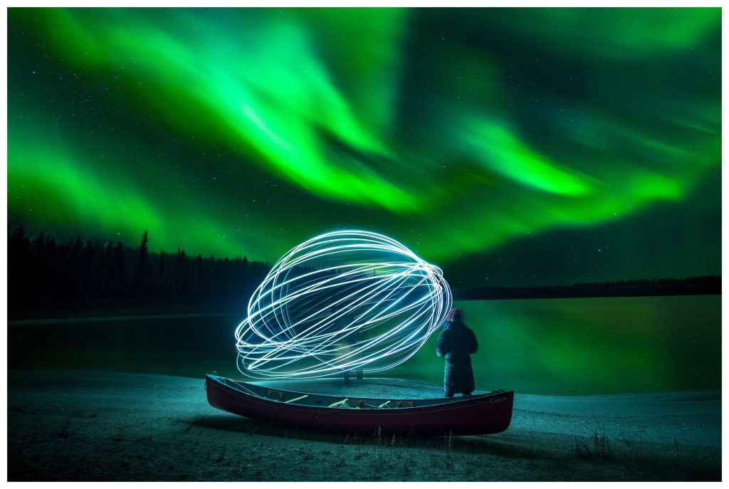 Person with light orb under auroras